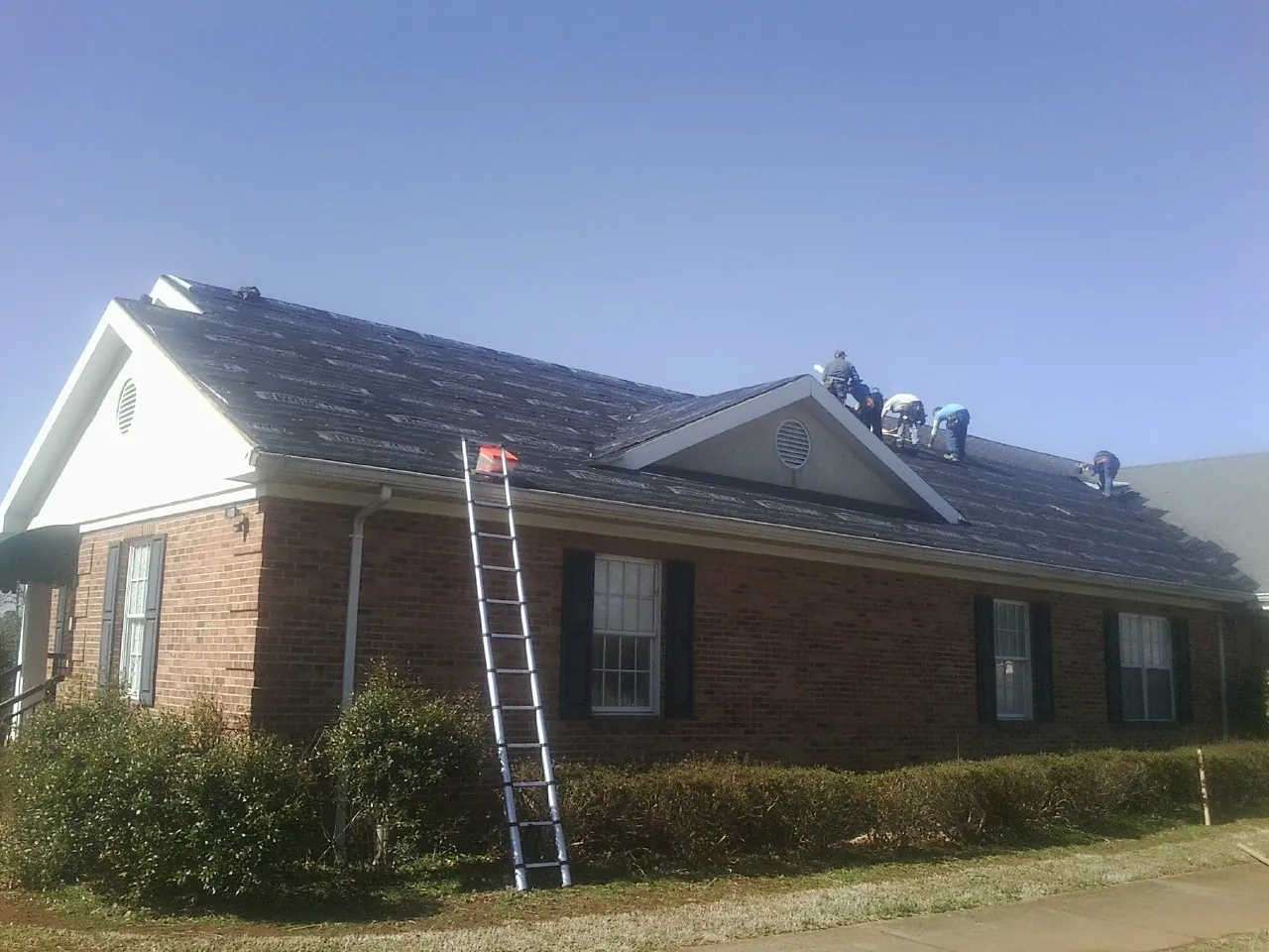Crew tearing shingles off a brick ranch roof with a ladder set — Metal Roof Repair work by our crew in Douglas