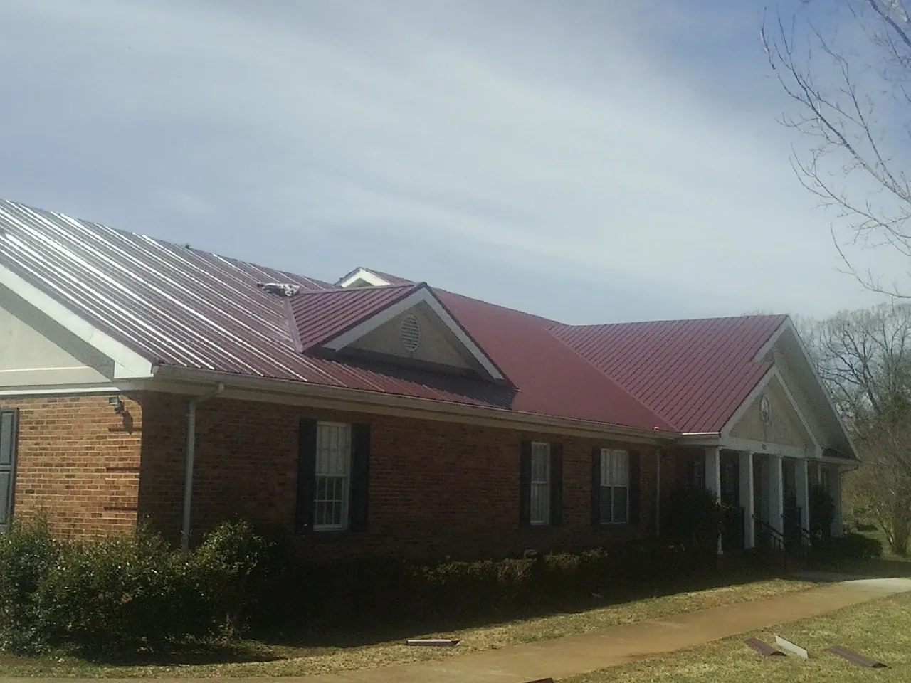 Red metal roof with gabled entries on a long brick building, from a Hail Damage Roof Repair job in Douglas